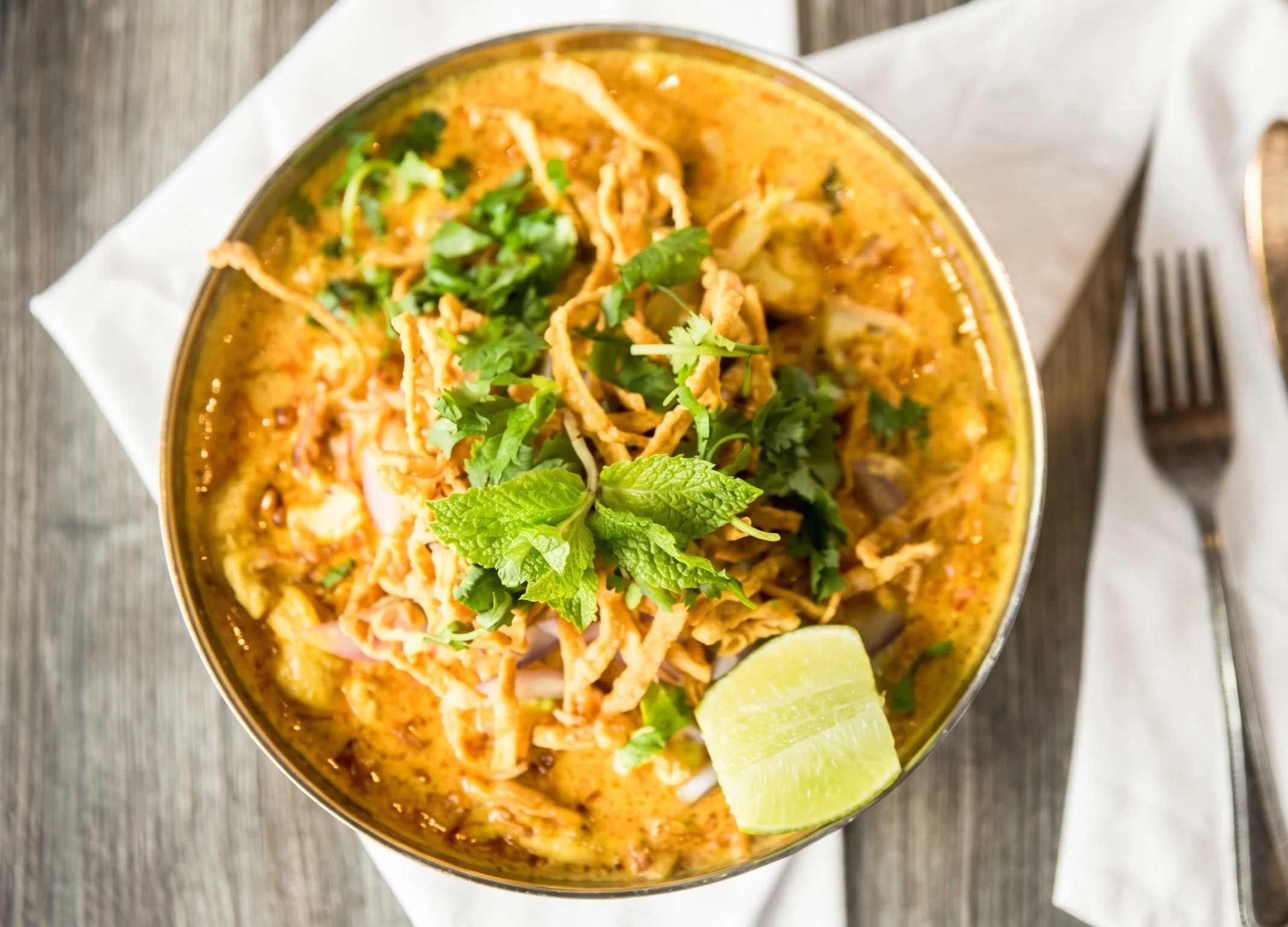 Bowl of Thai khao soi with crispy noodles and fresh herbs