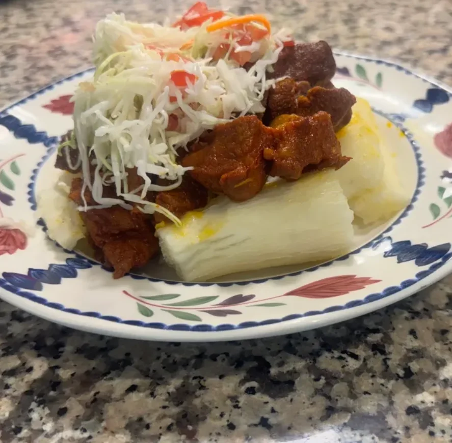 A plate of yucca topped with seasoned meat, shredded cabbage, and diced tomatoes, served on a decorative plate.