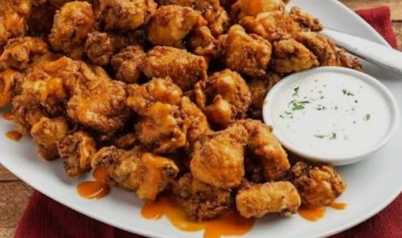 A serving platter filled with crispy fried chicken pieces, accompanied by a small bowl of dipping sauce.