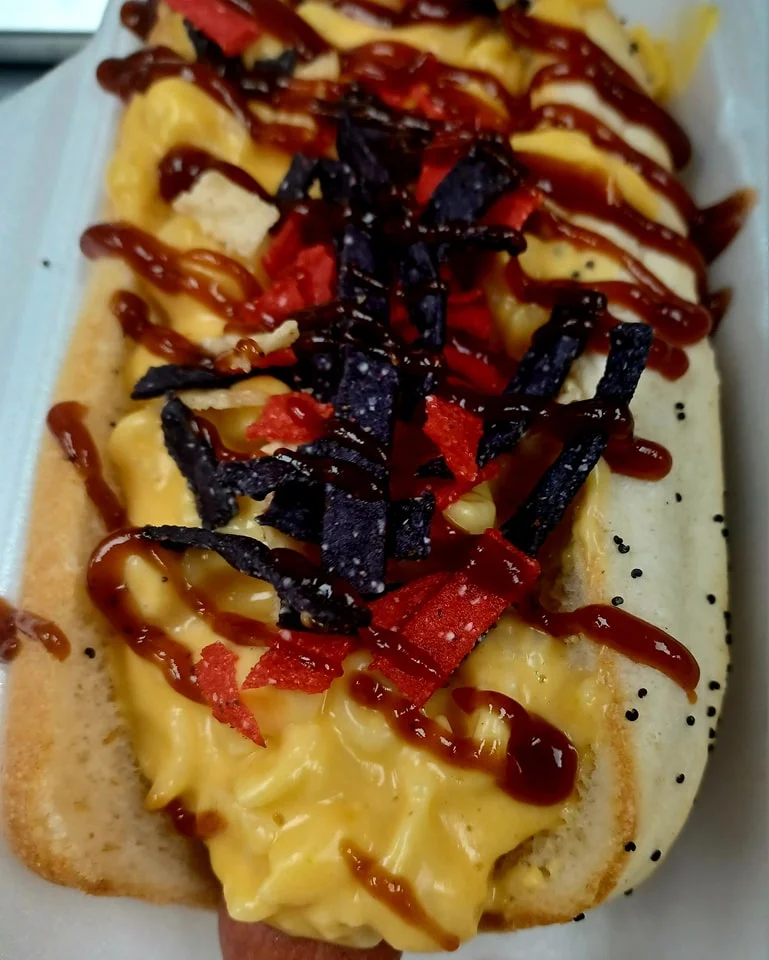 Loaded hot dog with mac and cheese, topped with chips and sauces