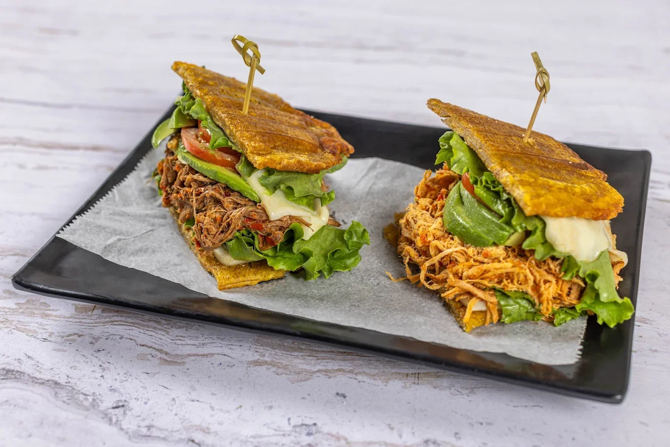 Two delicious patacón sandwiches, which use crispy fried green plantains instead of bread, filled with shredded meat, cheese, lettuce, and sauce.