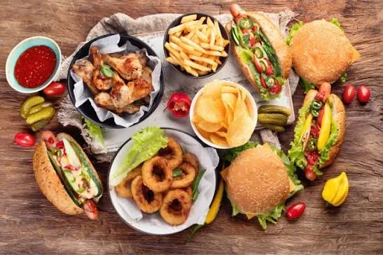 An assortment of fast food items, including burgers, fries, onion rings, chicken wings, and pickles, all beautifully arranged on a wooden surface.