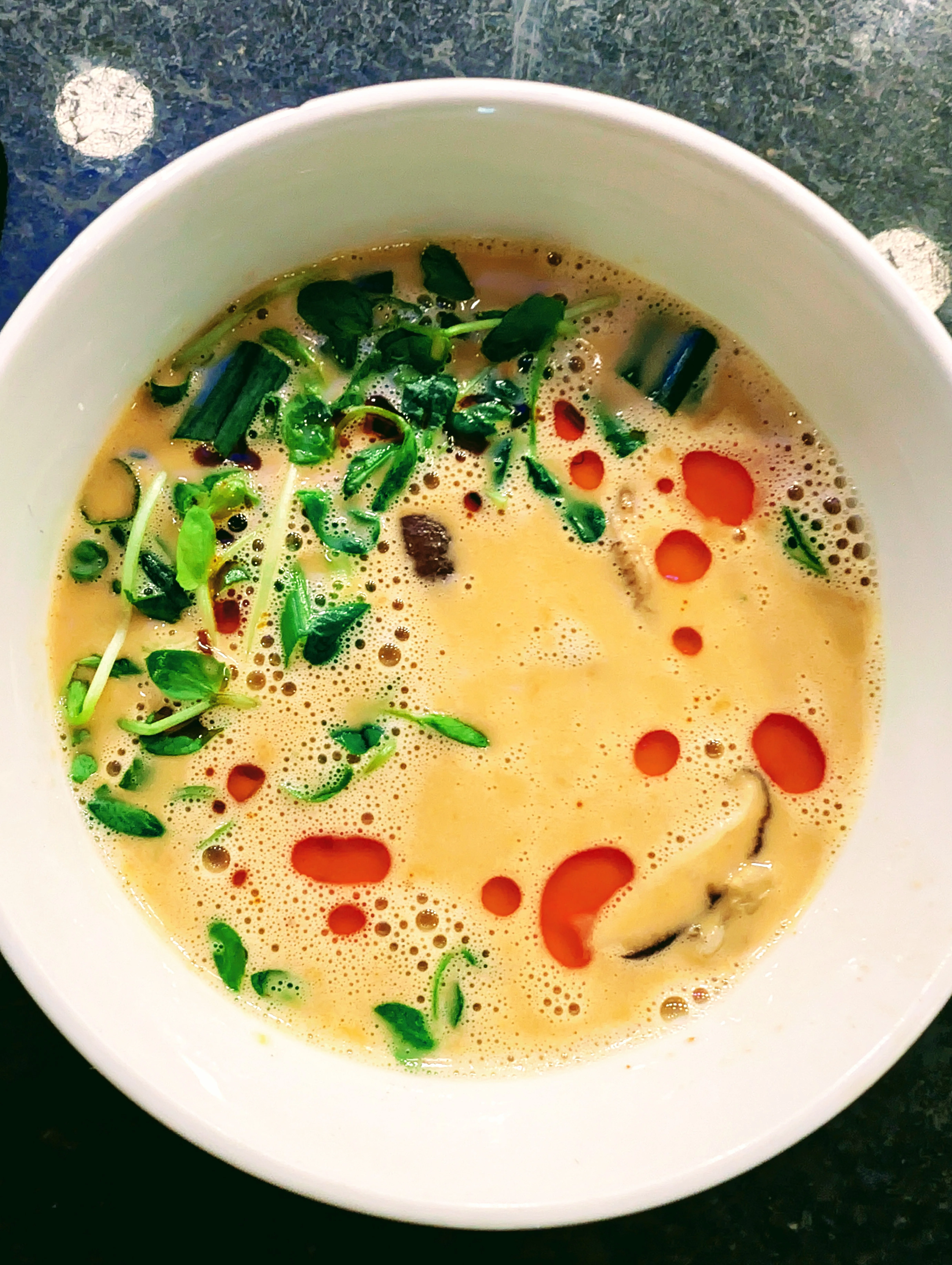 A bowl of creamy soup mixed with herbs and spices, displaying vibrant colors from the toppings.
