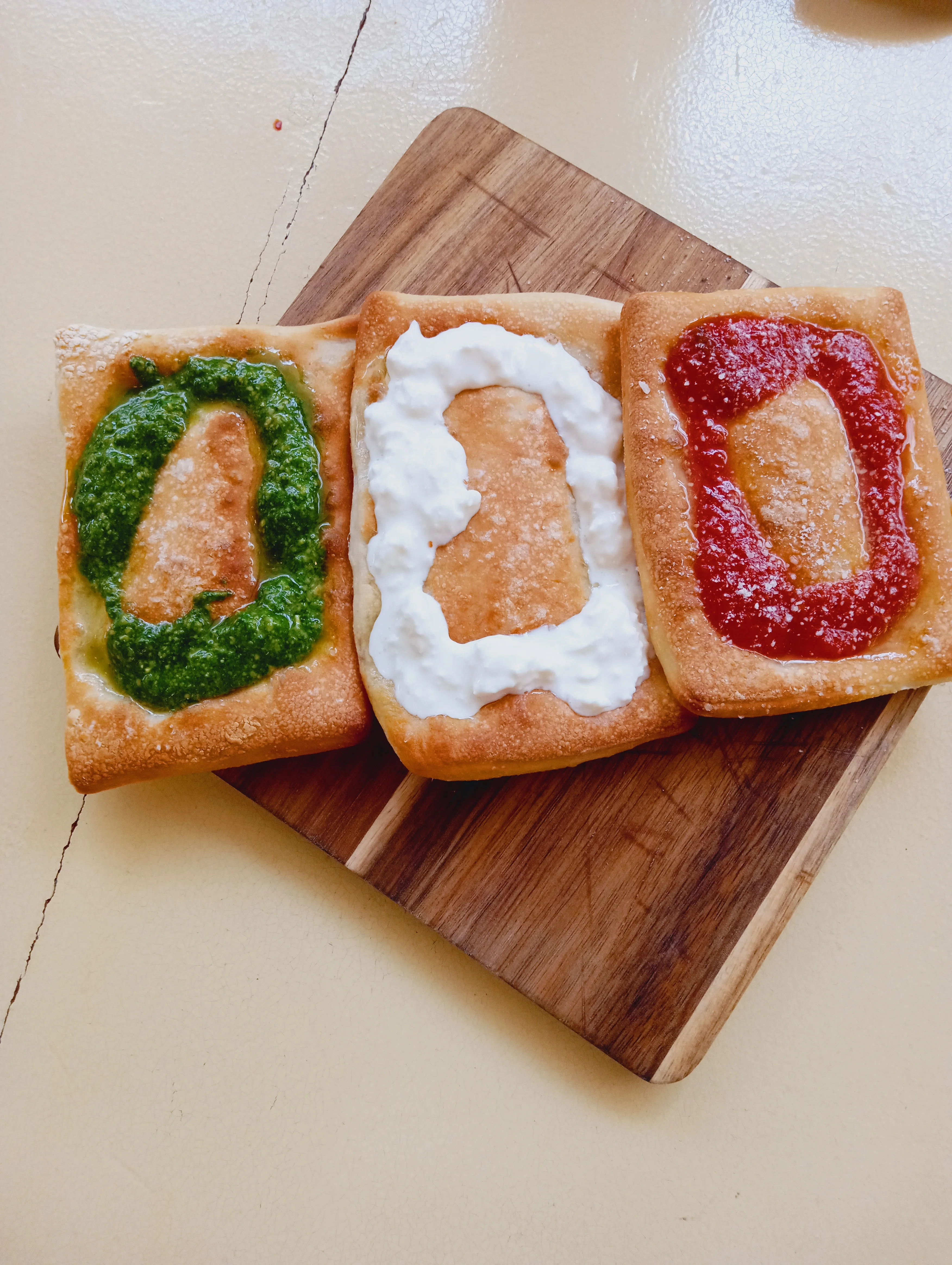 Three Mexican sopes topped with green sauce, cream, and red sauce