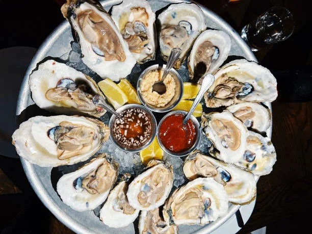 A plate of fresh oysters served on ice with lemon wedges.