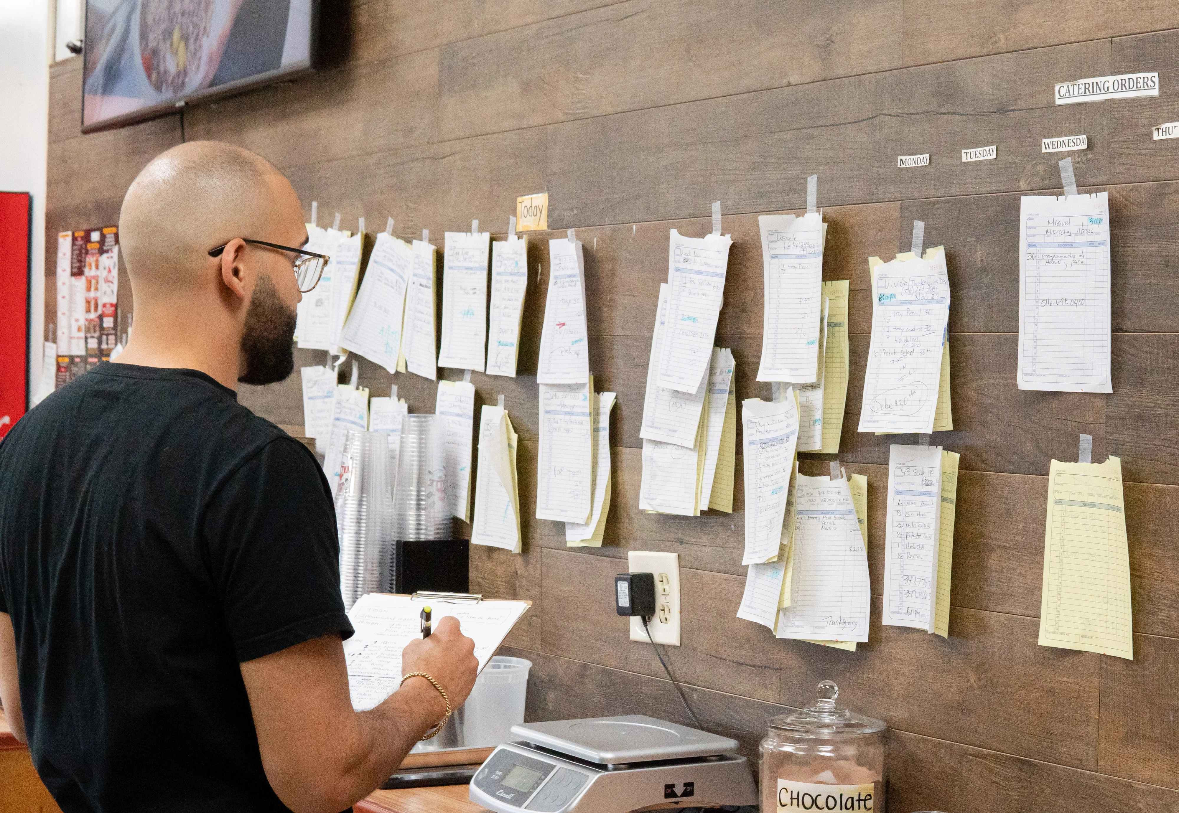 Restaurant staff reviewing catering orders on a busy kitchen wall