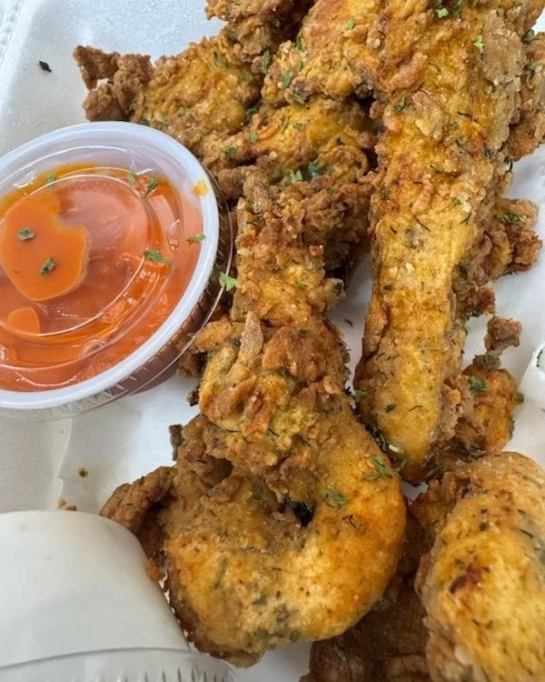 A serving of crispy fried chicken pieces accompanied by a small container of dipping sauce.