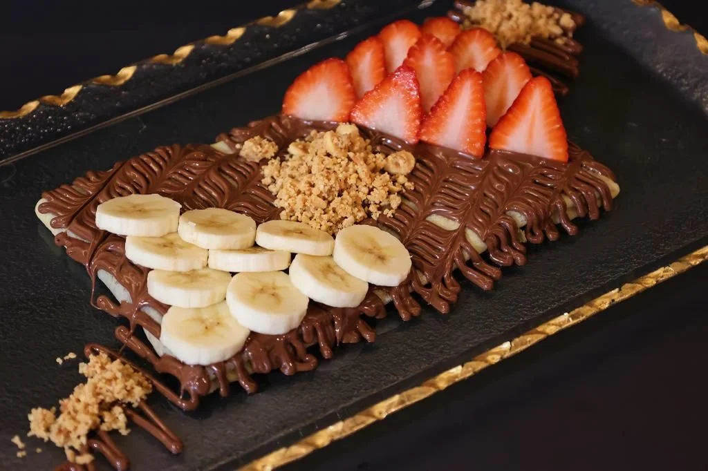 A beautifully presented chocolate dessert topped with strawberries and banana slices on a black plate.