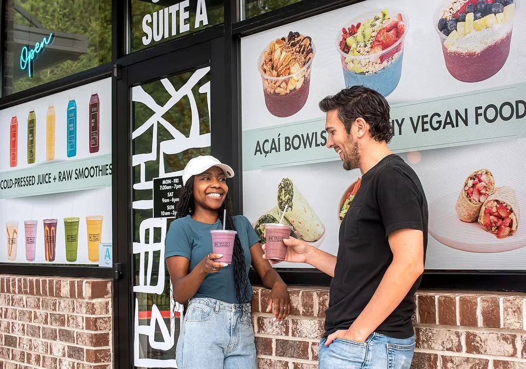 Two friends enjoying smoothies outside a vibrant juice bar