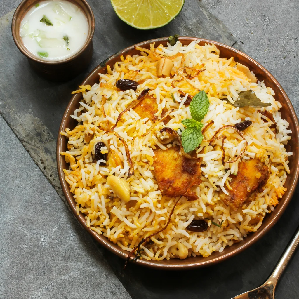 Delicious chicken biryani served with raita and lime