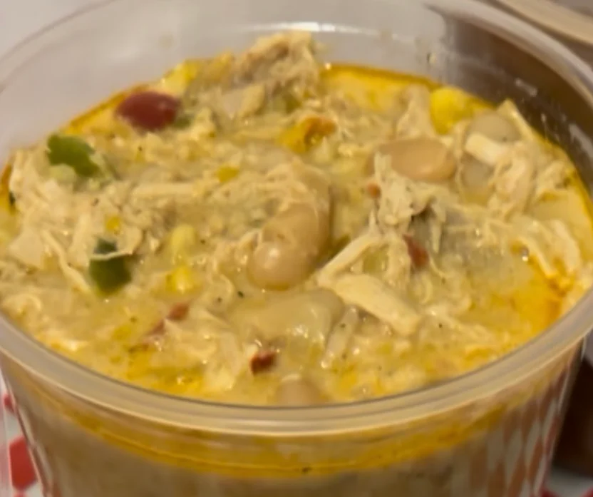 A cup filled with a creamy mixture that includes shredded chicken, corn, and diced vegetables.