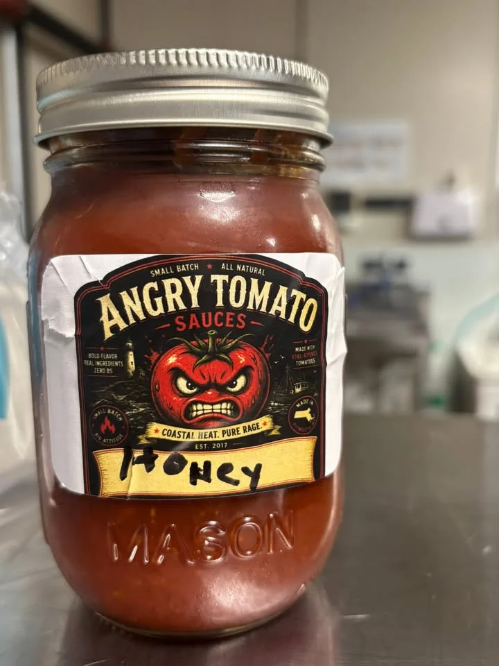 A jar of sauce labeled as 'Angry Tomato' with a bold graphic, indicating it's a honey flavor and reflects a rustic production style.