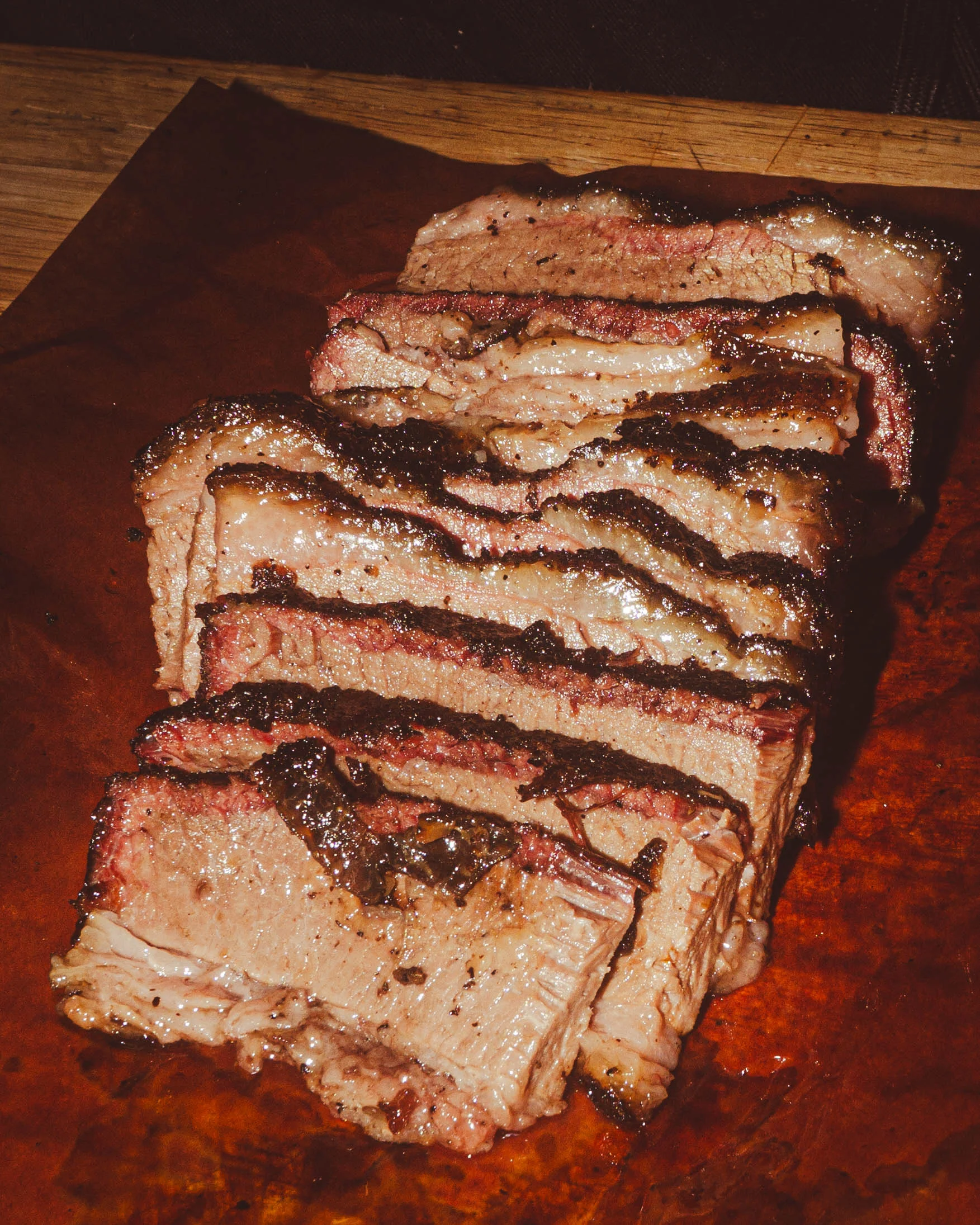 Sliced brisket on a wooden board, showcasing juicy layers and smoky crust.