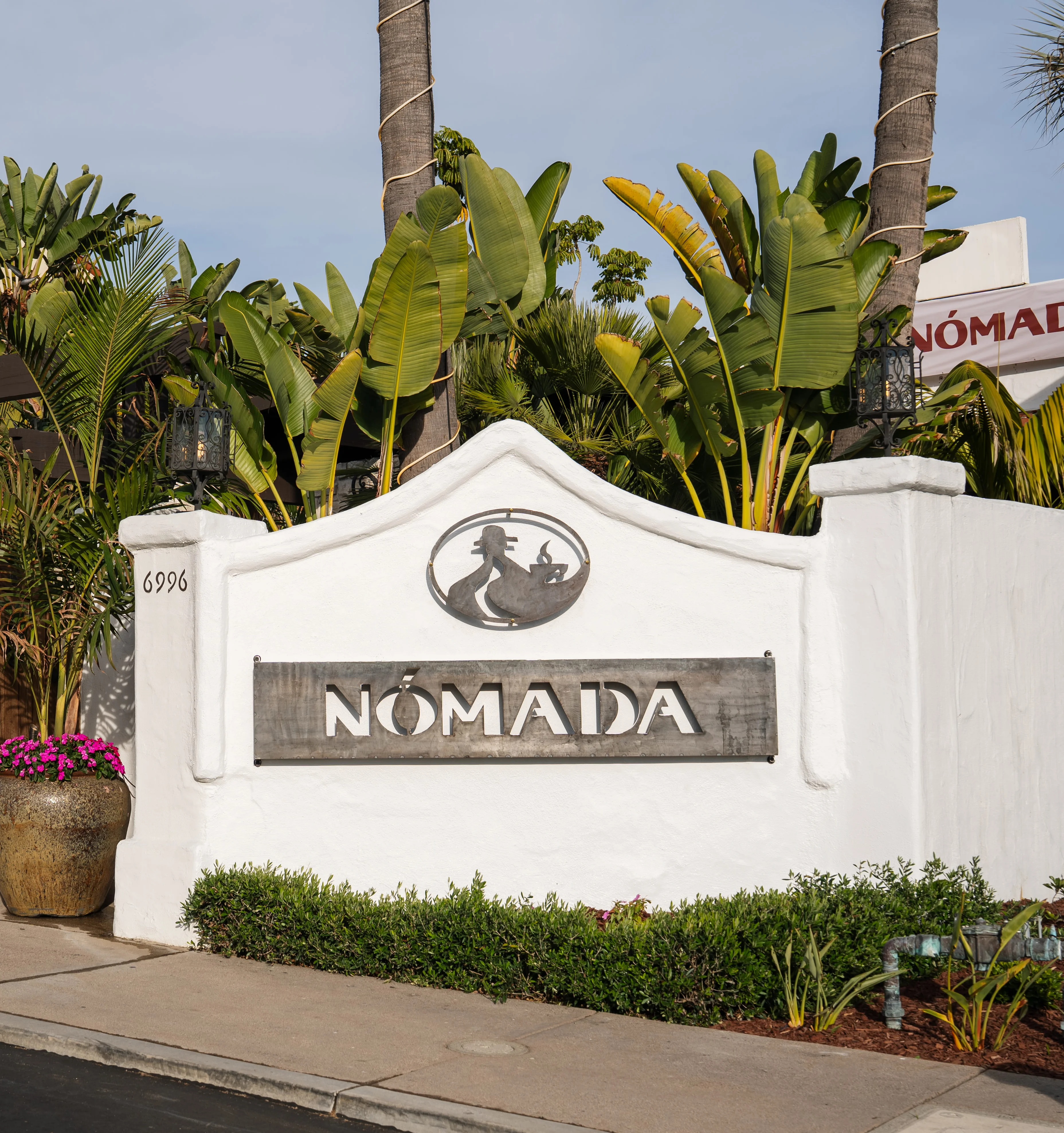 Entrance of Nómada restaurant with tropical plants and wooden gate