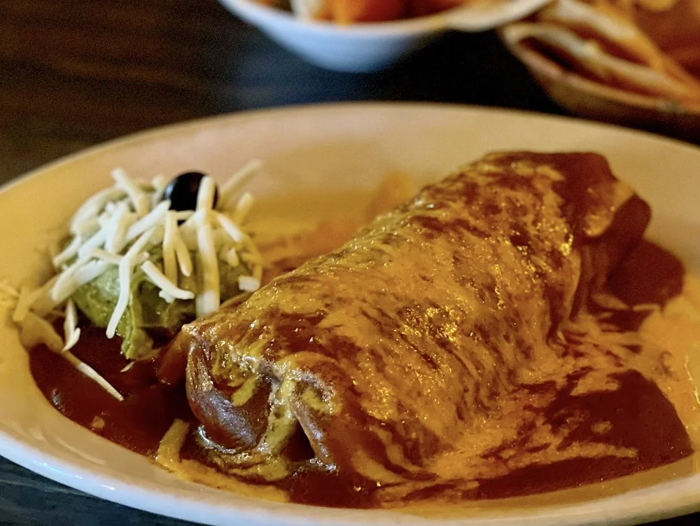 A burrito topped with enchilada sauce and melted cheese