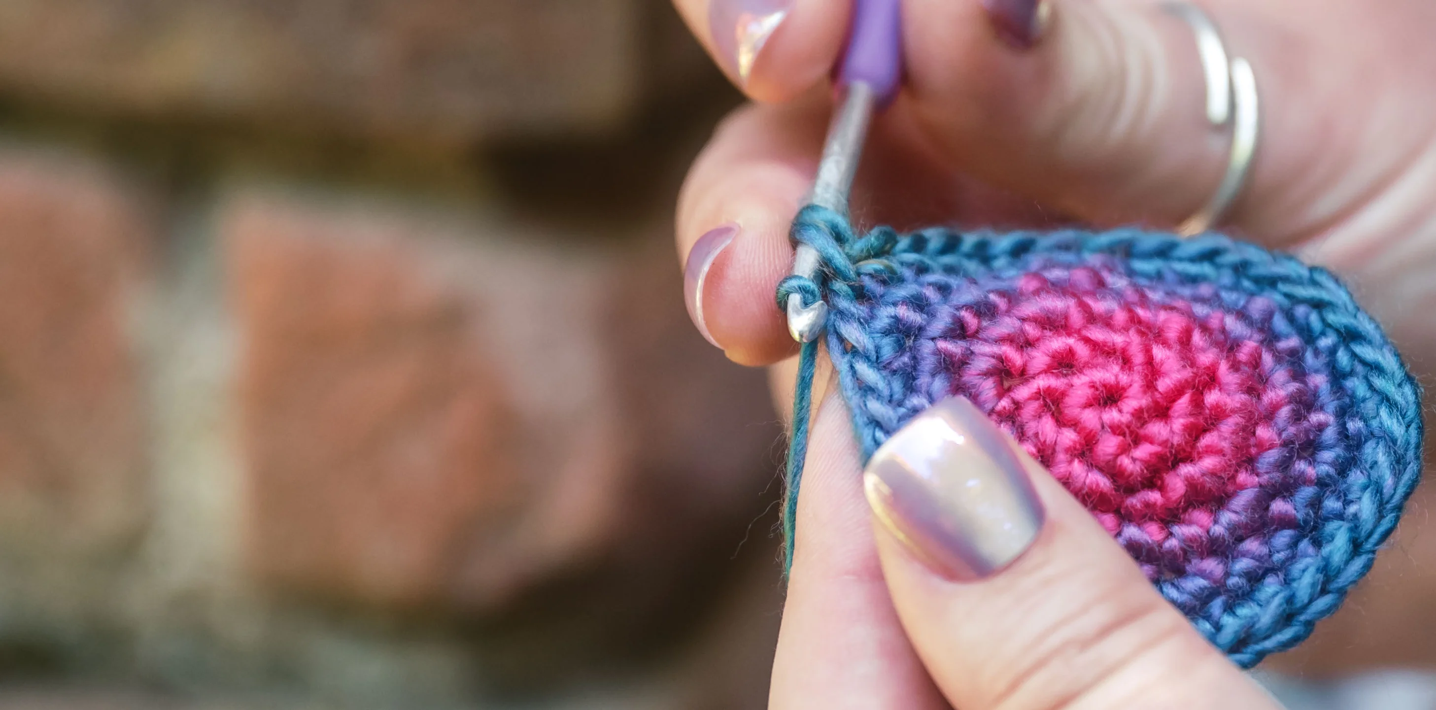 Person knitting with blue yarn and a cup of tea nearby