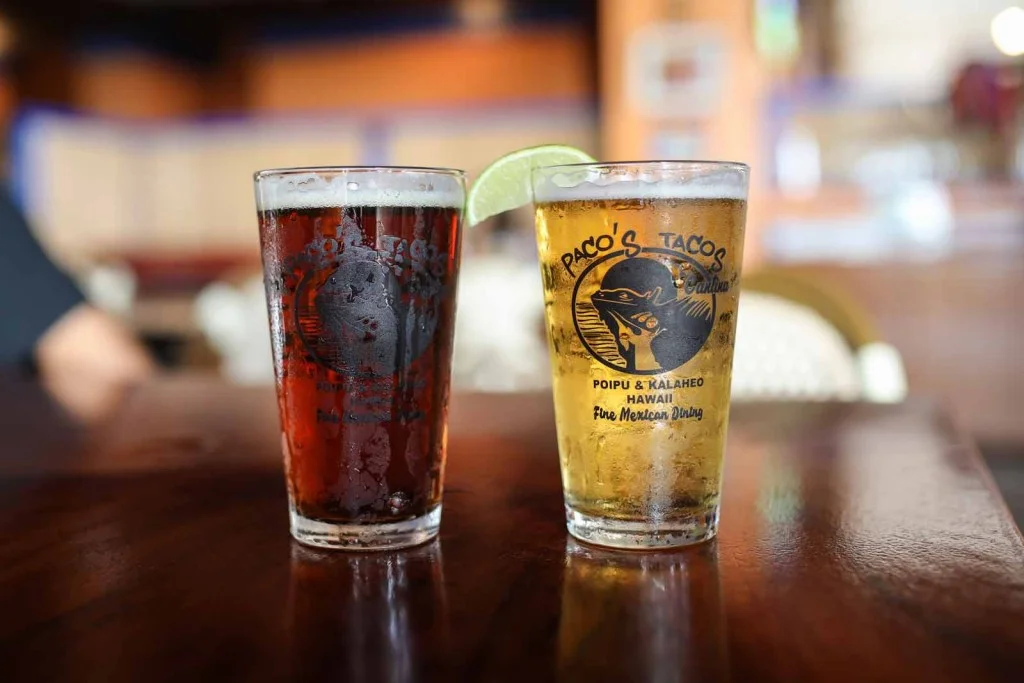 Two glasses of beer with lime in a vibrant restaurant setting