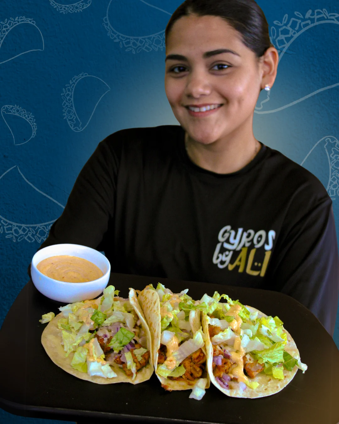 A Gyros by Ali employee holding a platter of mediterranean tacos