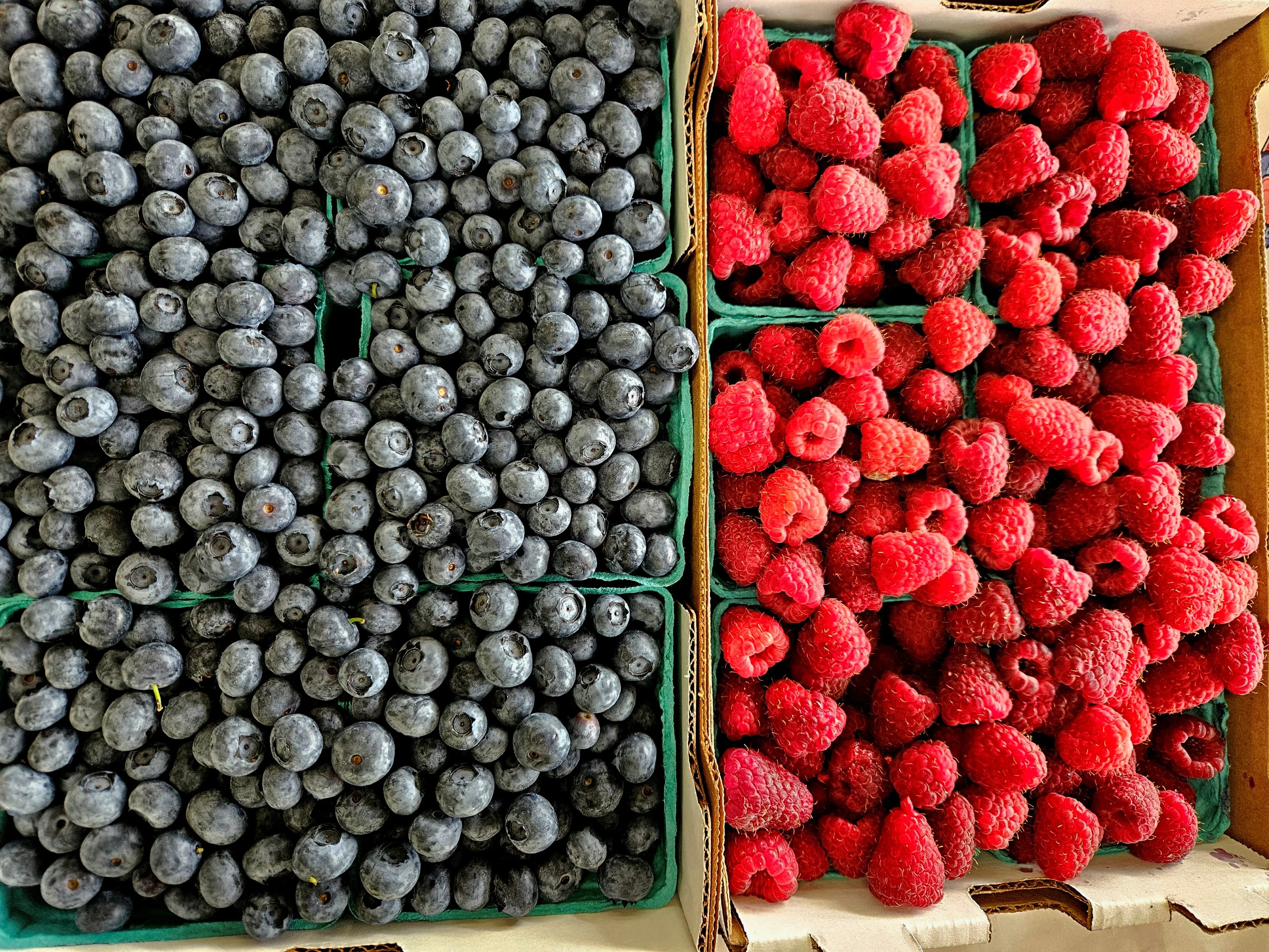 A vibrant market display featuring a variety of fresh fruits and vegetables, including apples, oranges, and greens, neatly organized on wooden tables.