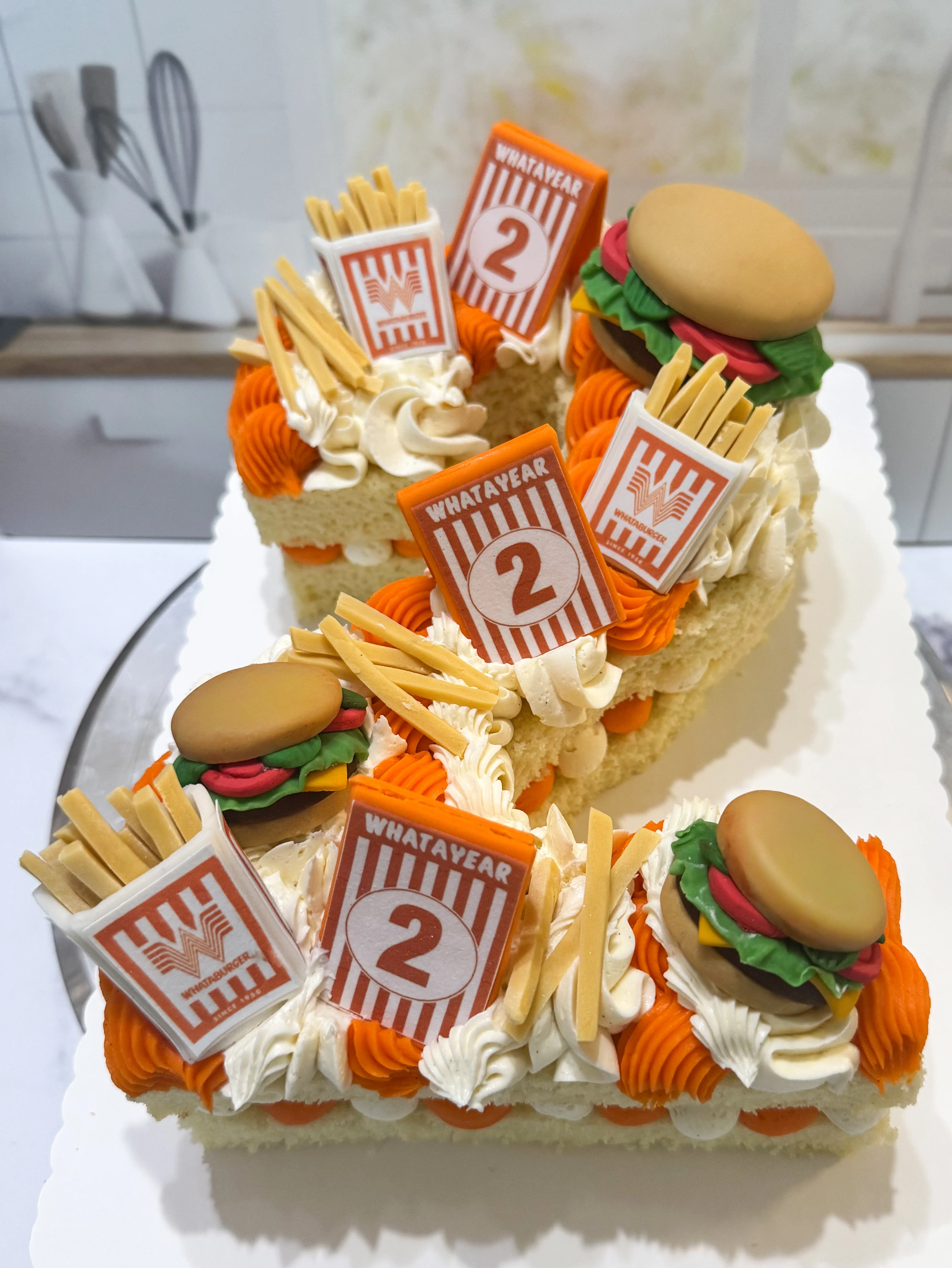 A creatively decorated cake designed to resemble fast food, featuring elements like fries, burgers, and fun decorations for a two-year celebration.