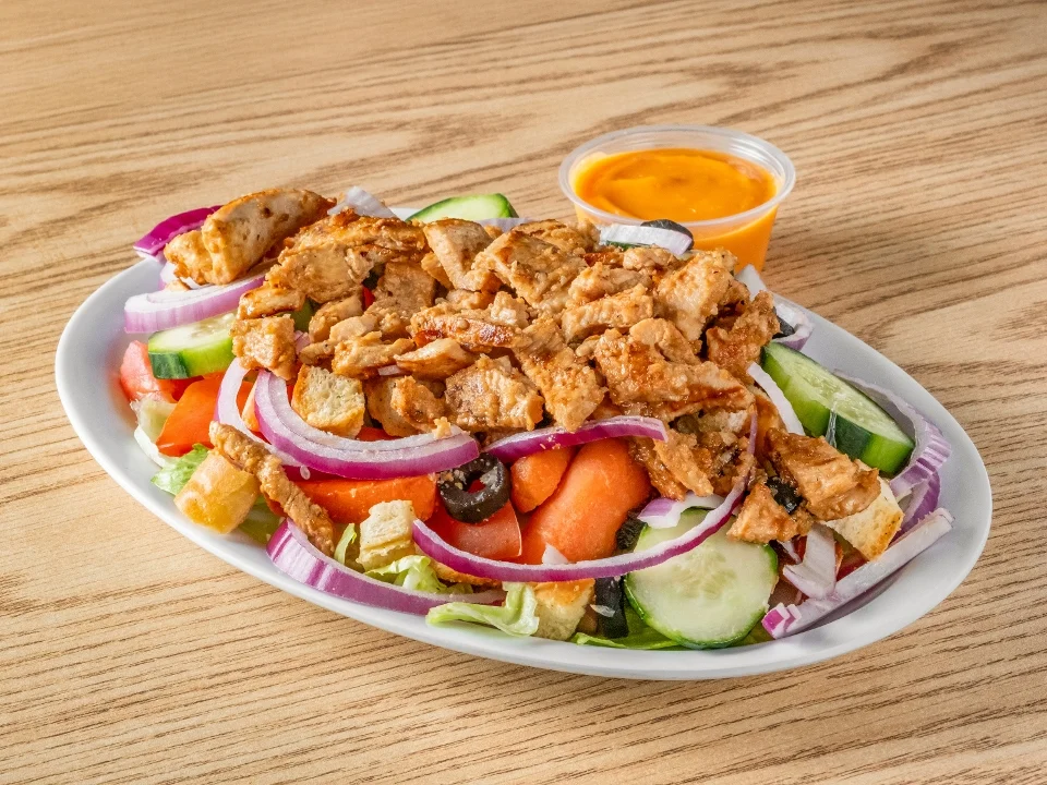 A colorful salad topped with grilled chicken, accompanied by various vegetables and a small cup of dressing.