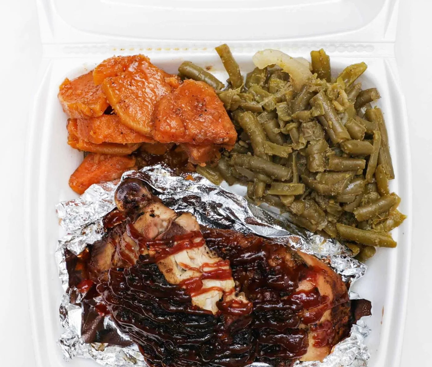 A takeout container featuring a chicken wing, rice, black beans, and macaroni and cheese, creating a delicious combo plate.