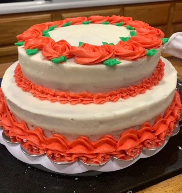 Two-tiered cake decorated with orange frosting and green accents