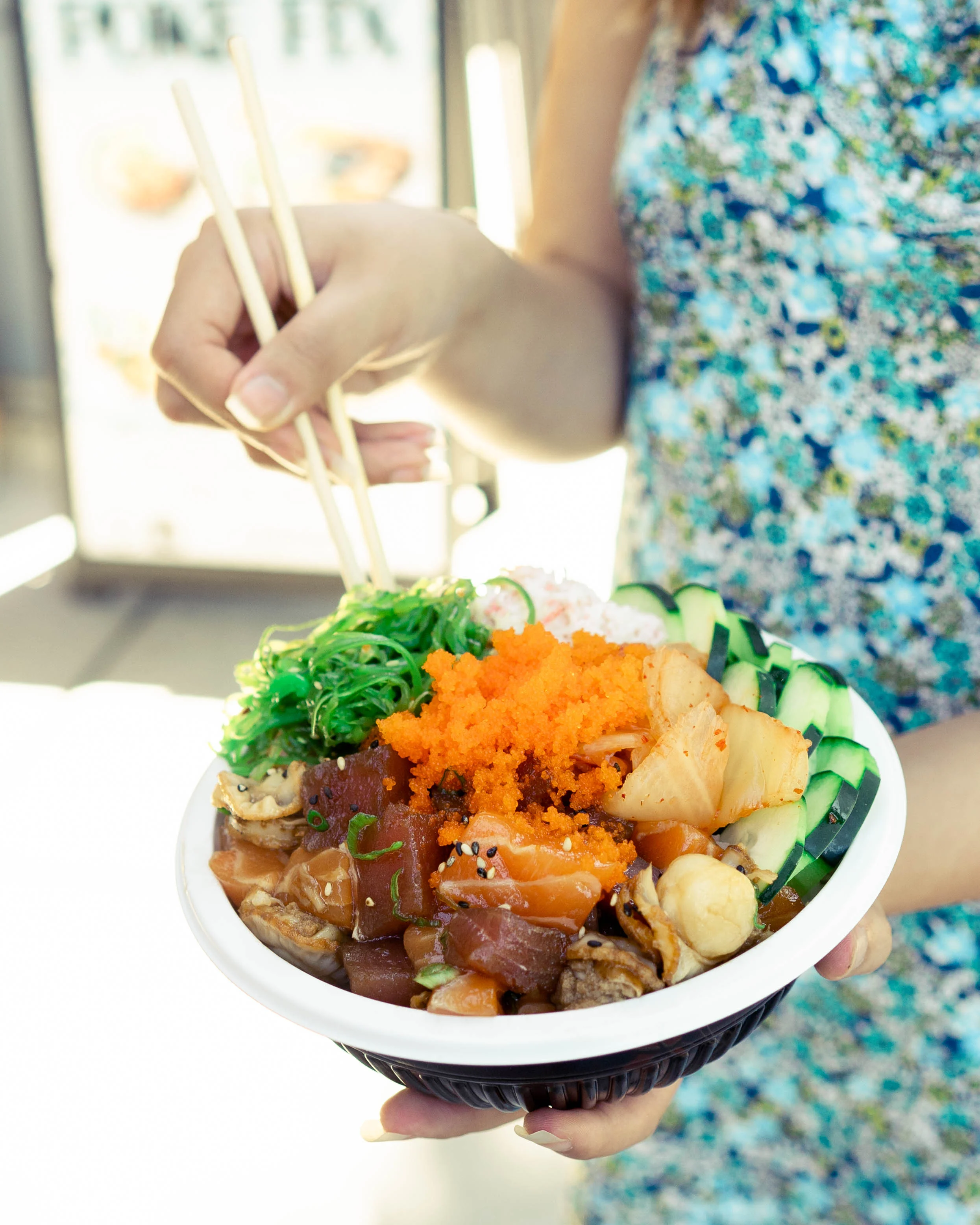 A colorful poke bowl with seafood, vegetables, and chopsticks.