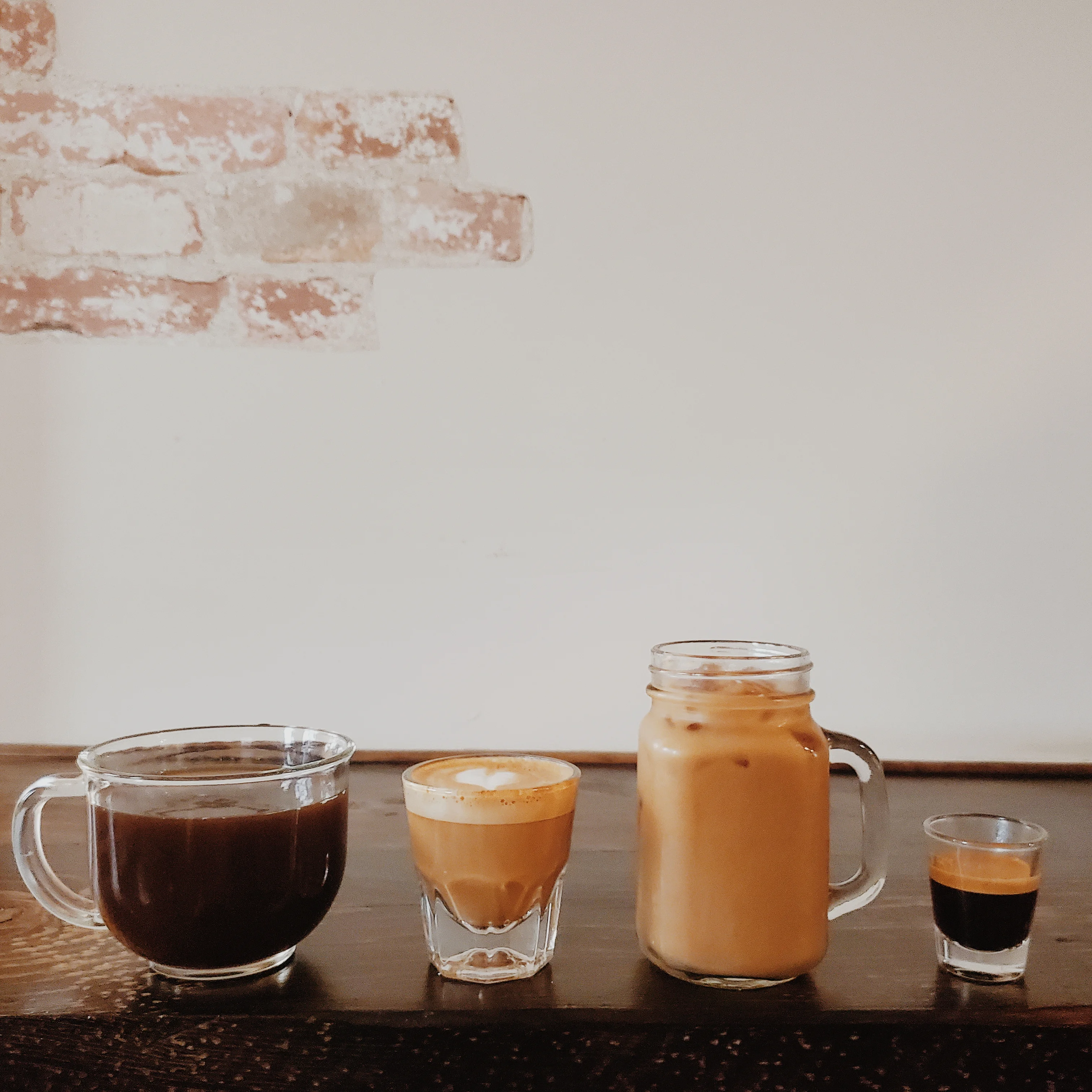 A selection of coffee beverages arranged on a wooden surface, including a cup of black coffee, an espresso shot, an iced coffee, and a small glass of concentrated coffee.