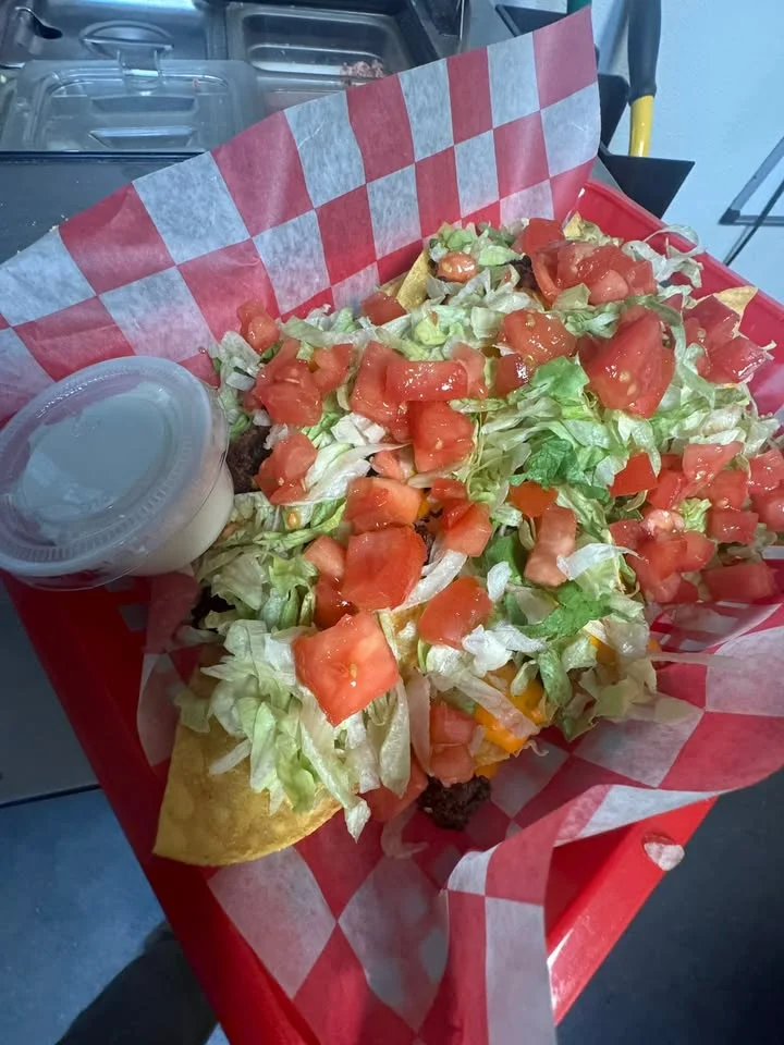 A basket of loaded tater tots topped with cheese, meat, and other savory ingredients, served in a checkered container.