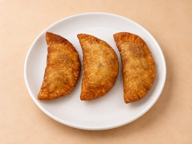 Three golden-brown empanadas arranged on a white plate.