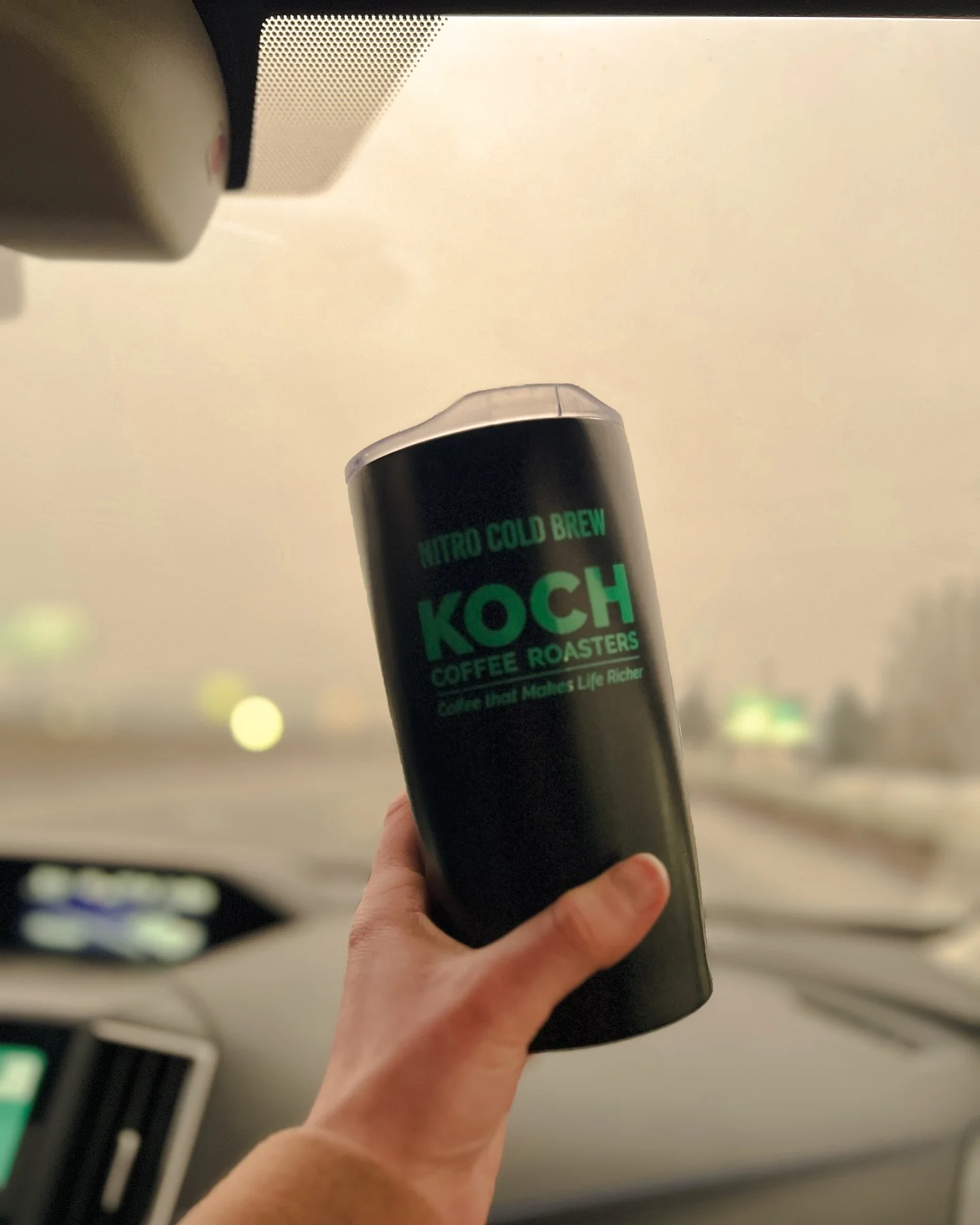 Hand holding a nitro cold brew coffee in a car