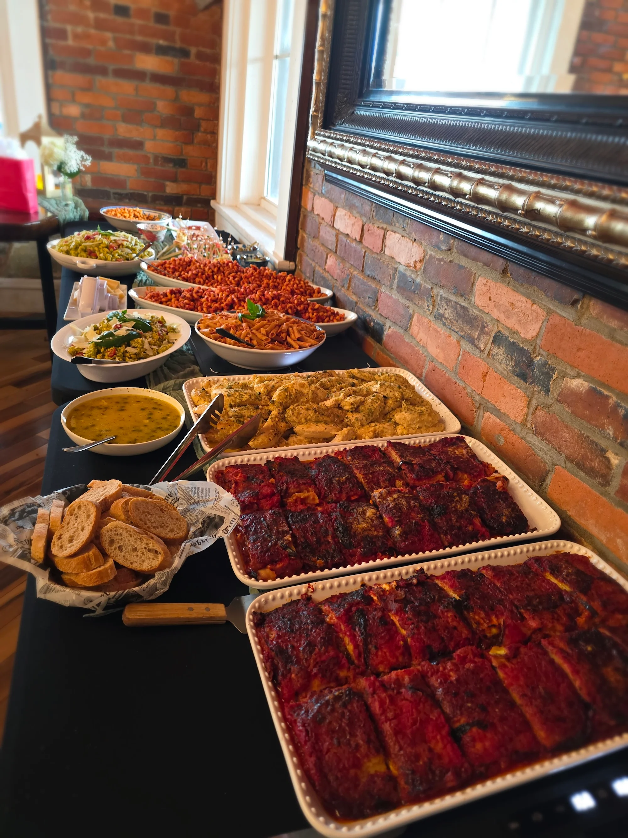 A buffet table filled with a variety of dishes including pasta, salads, and meatloaves, alongside a basket of bread.