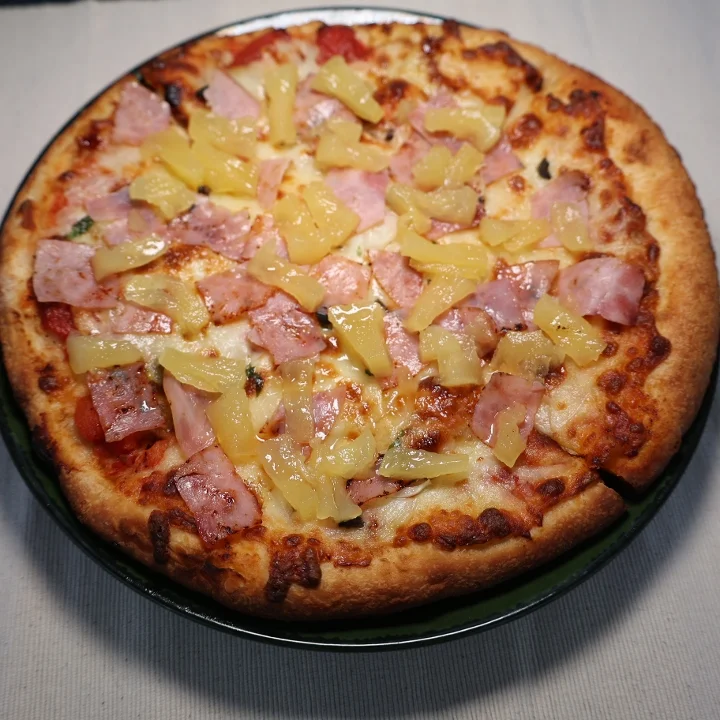 A Hawaiian pizza topped with chunks of ham and pineapple on a well-baked crust.