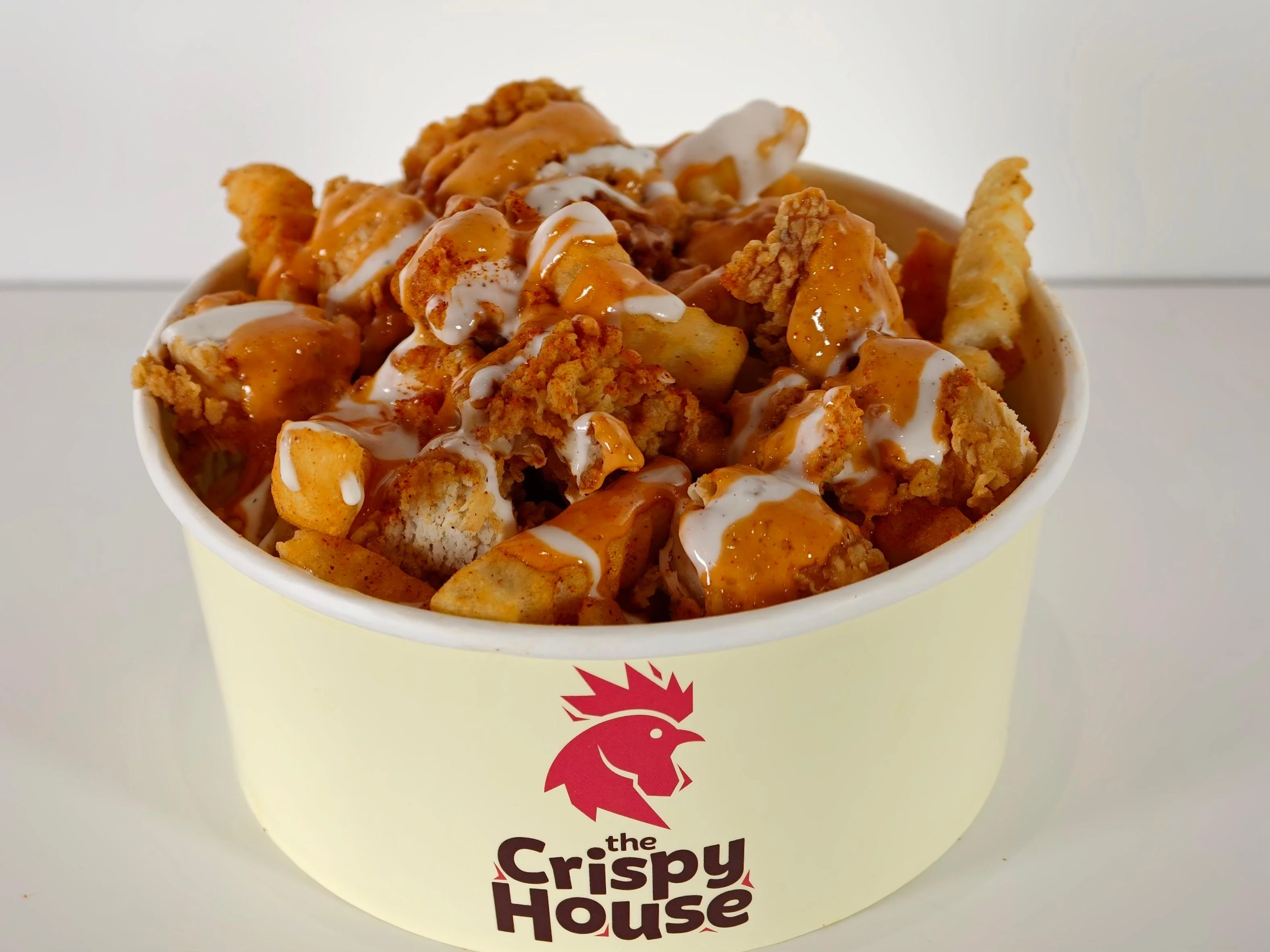 A bowl filled with fried chicken pieces, crinkle fries, and drizzled sauces, served in a branded container.