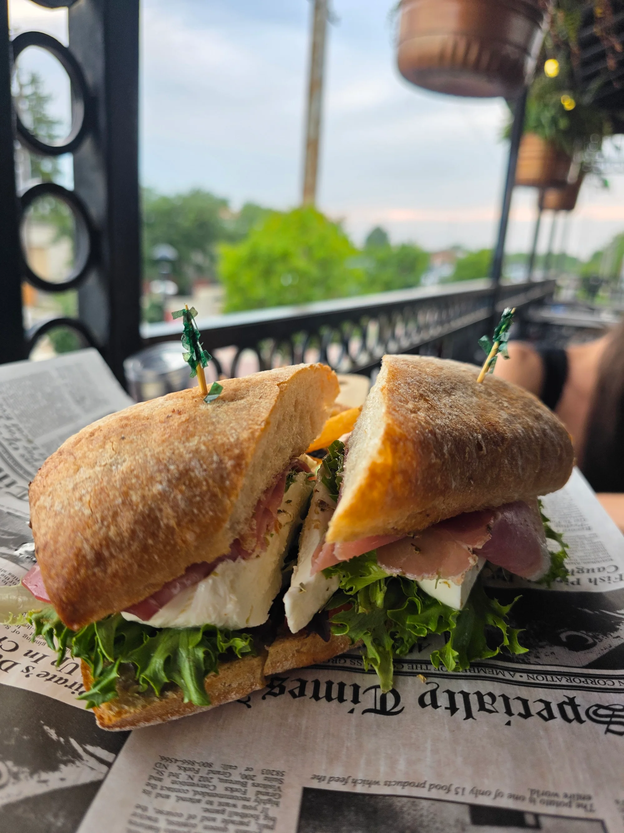 A freshly made sandwich with layers of ham, cheese, and lettuce, served on newspaper under a clear sky.
