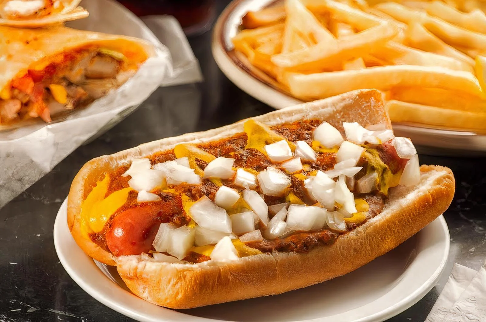 A hot dog topped with mustard and diced onions, served on a bun next to a plate of French fries.