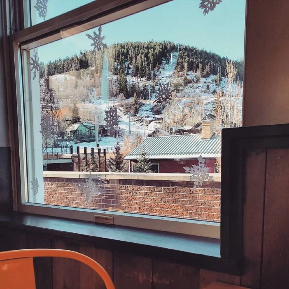 A view from a window showcasing a snow-covered landscape with trees and houses, decorated with snowflake patterns on the glass.