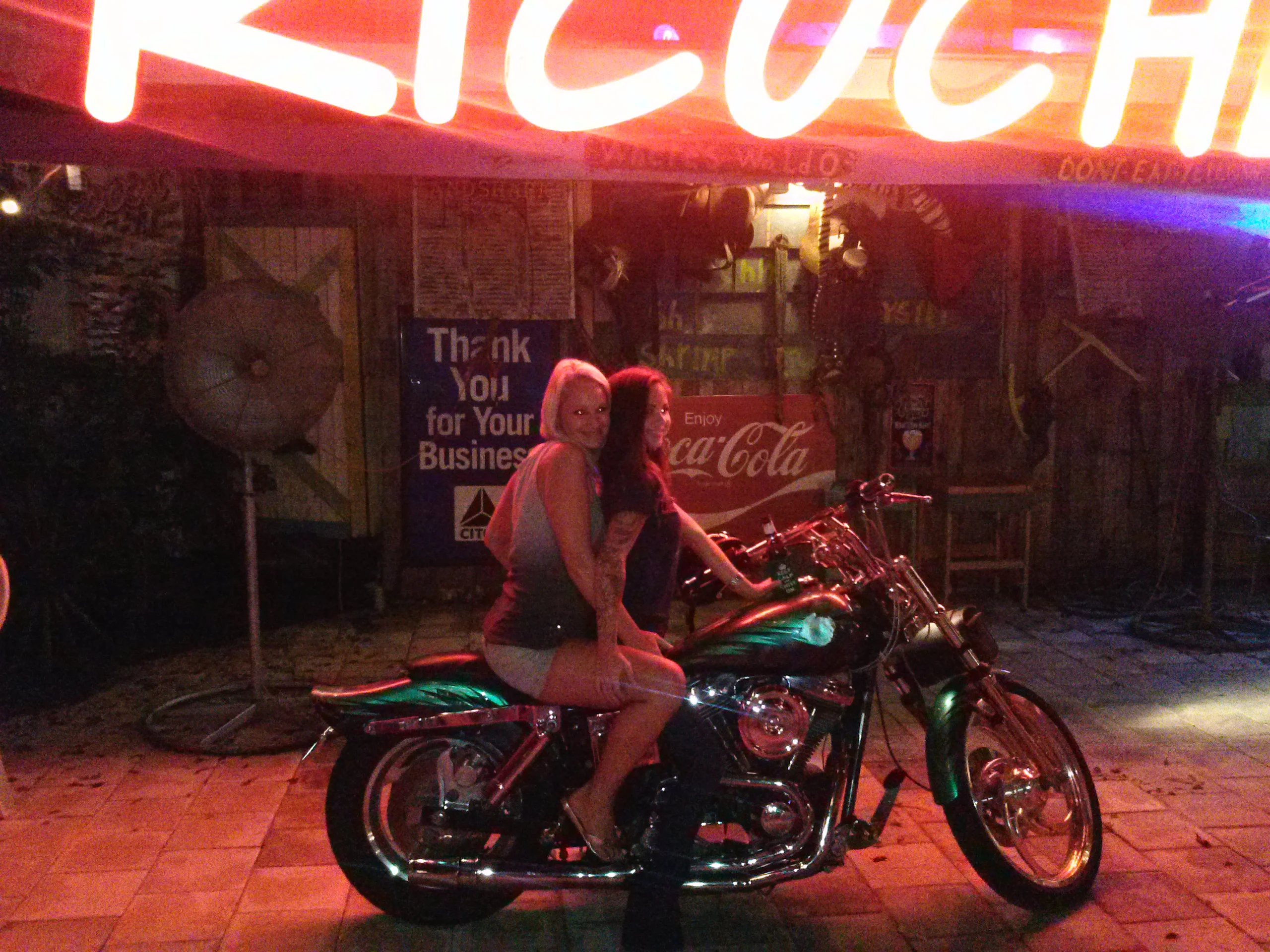 Two women posing on a motorcycle outside a vibrant restaurant at night