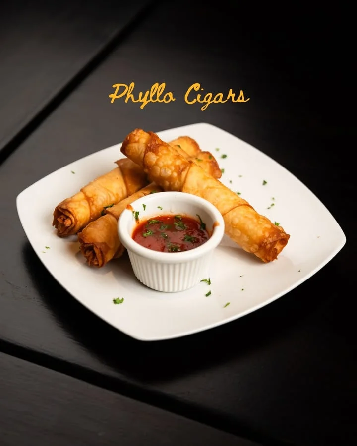 A plate of phyllo cigars served with a dipping sauce, garnished with herbs.