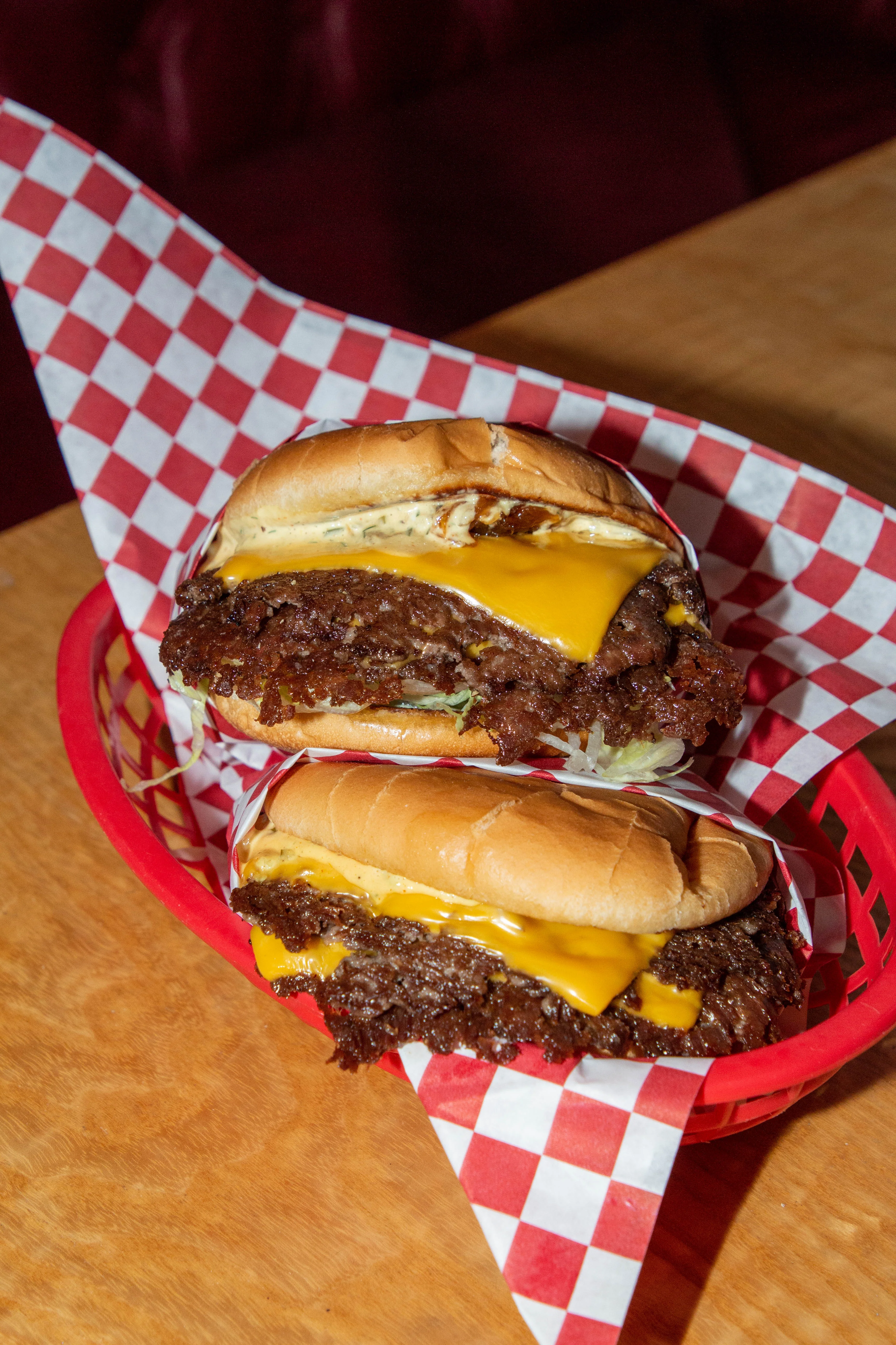 Two cheeseburgers with melted cheese in a red basket with checkered paper.