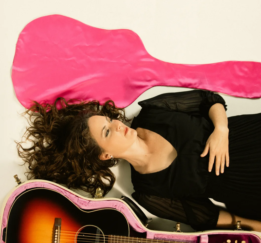 Woman lying with guitar and pink fabric, artistic portrait