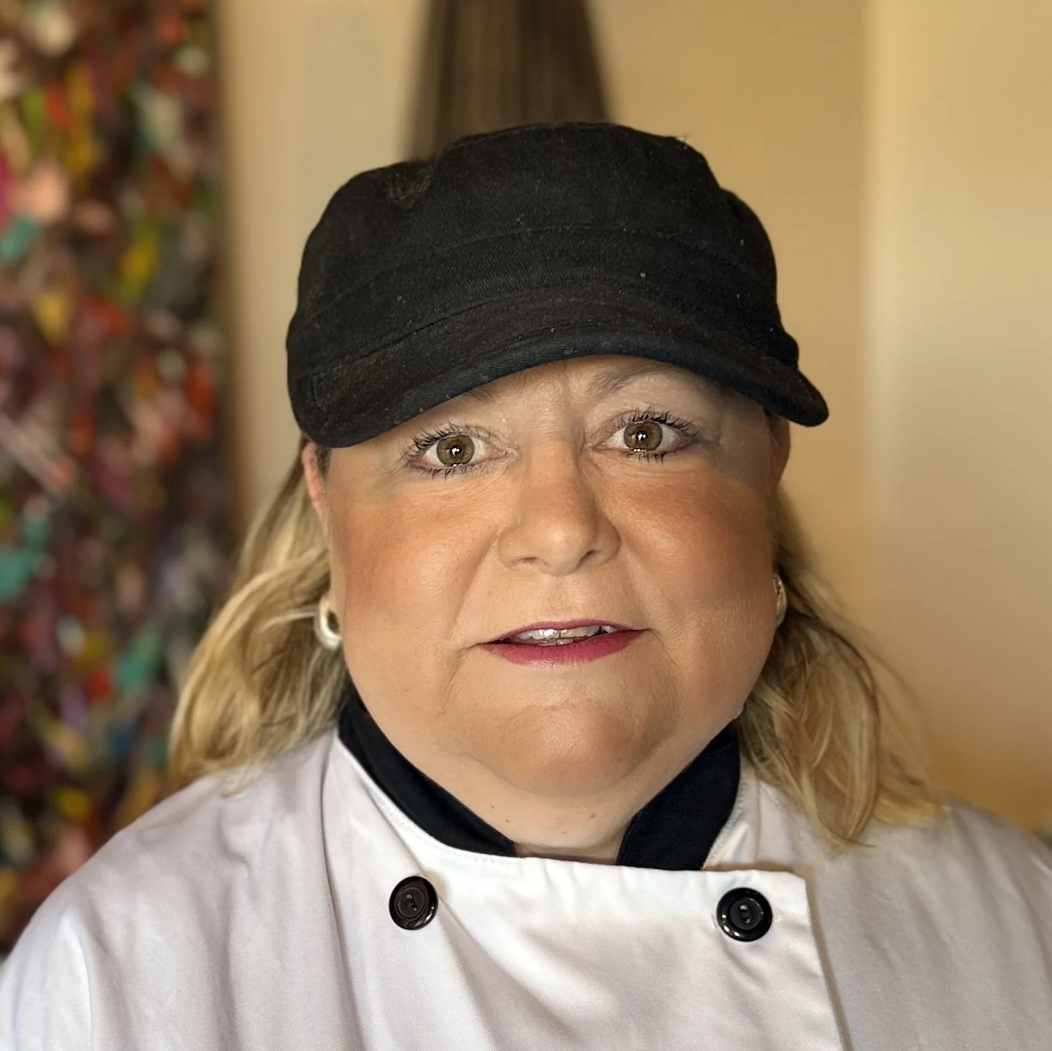 Chef in a white coat and black cap smiling in a restaurant setting