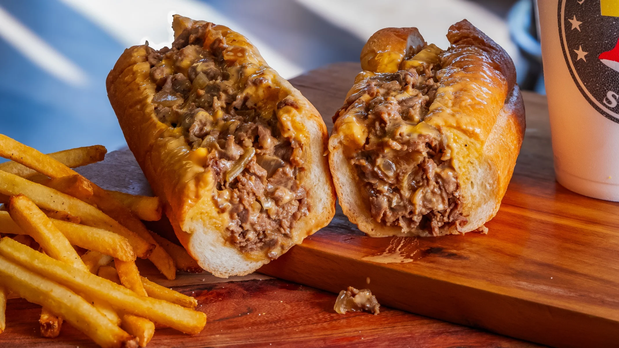 A hearty sub sandwich filled with beef, cheese, and vegetables, accompanied by a side of crispy French fries on parchment paper.