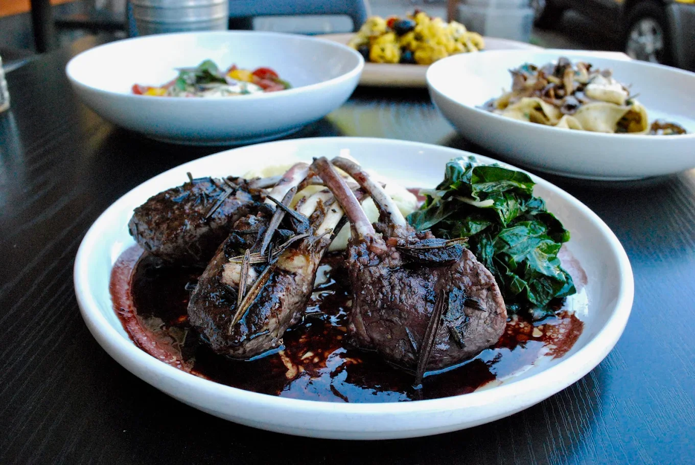 A plate featuring grilled lamb chops served with a rich sauce, accompanied by a side of greens and creamy mashed potatoes.