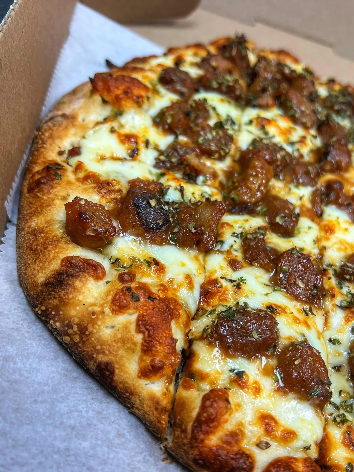 A pizza with melted cheese on top, garnished with seasoned meat chunks and herbs.