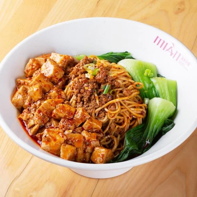 Bowl of noodles with meat and garnishes, served in a vibrant dish.