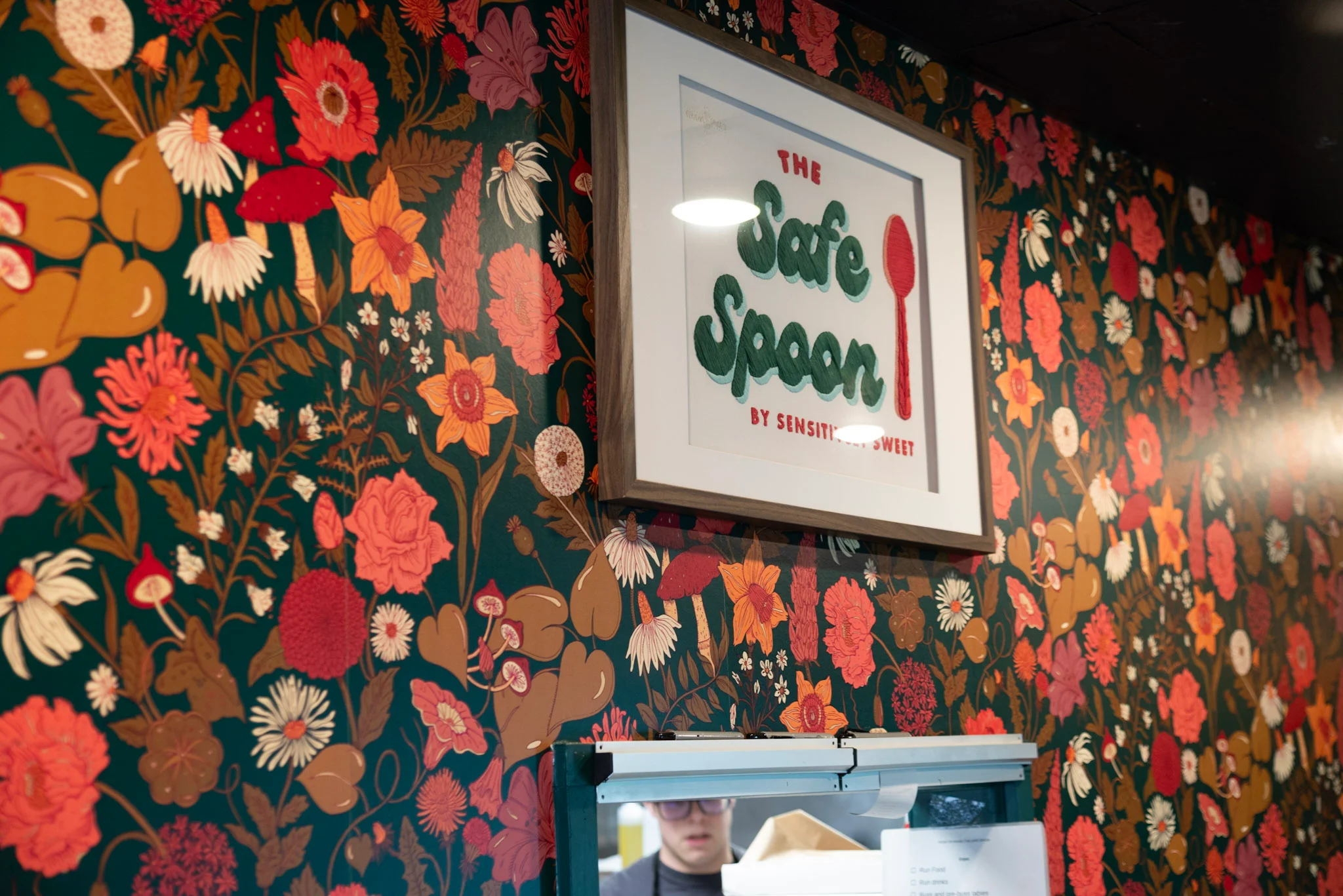 A vibrant floral wallpaper with a framed sign that reads 'The Safe Spoon', adding a lively touch to the space.