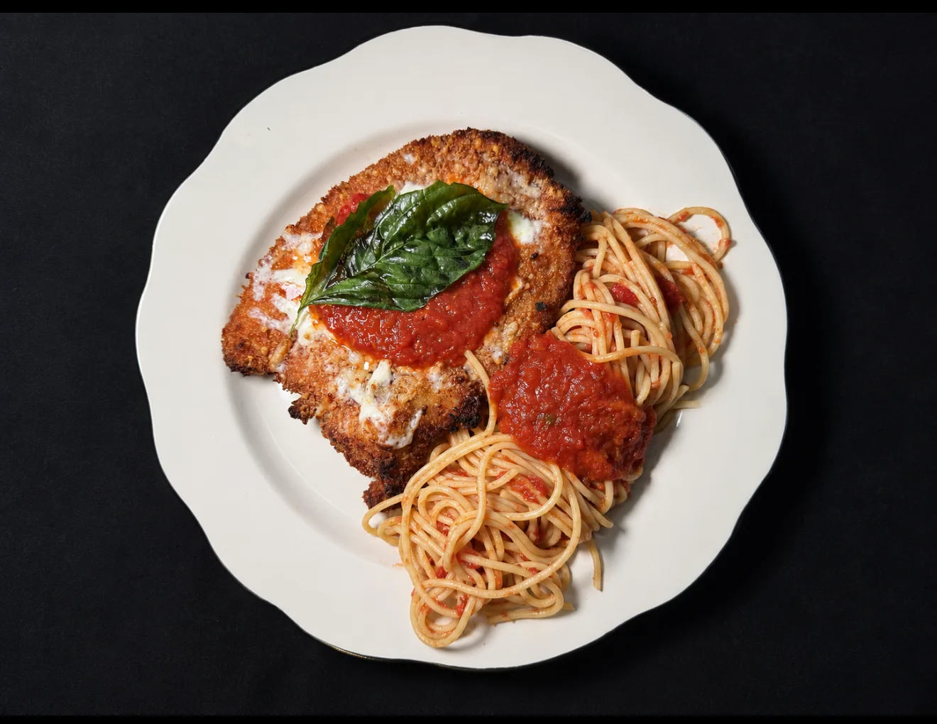 Crispy chicken parmesan with spaghetti marinara on a white plate
