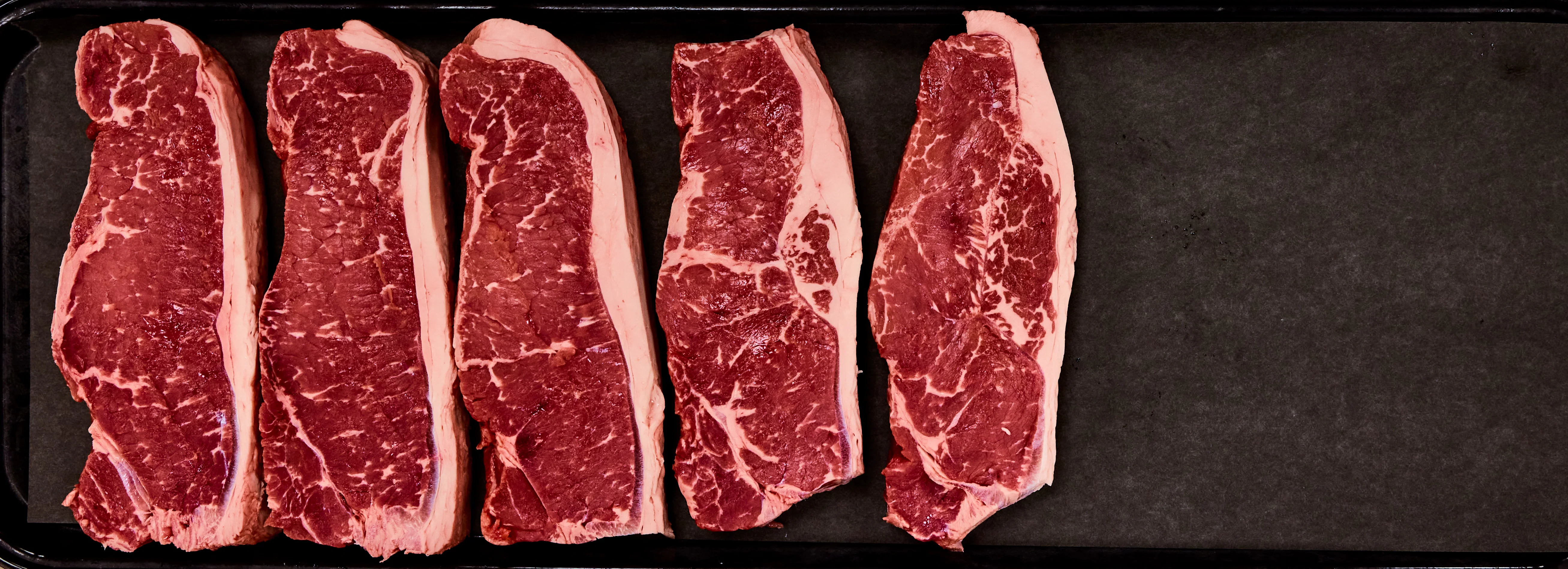 Raw marbled ribeye steaks arranged on a black tray